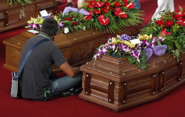 A man sits next to the coffins of victims of a coach crash during the funeral service at the Monteruscello Palasport