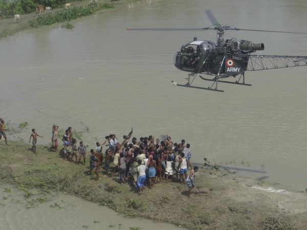 Flood-affected people gather under an Indian Army helicopter carrying relief materials at the flooded area of Sunipur district in Assam