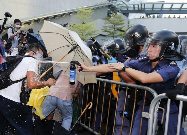 A riot policeman uses pepper spray during clash with protesters, as tens of thousands of protesters block the main street to the financial Central district outside the government headquarters in Hong Kong