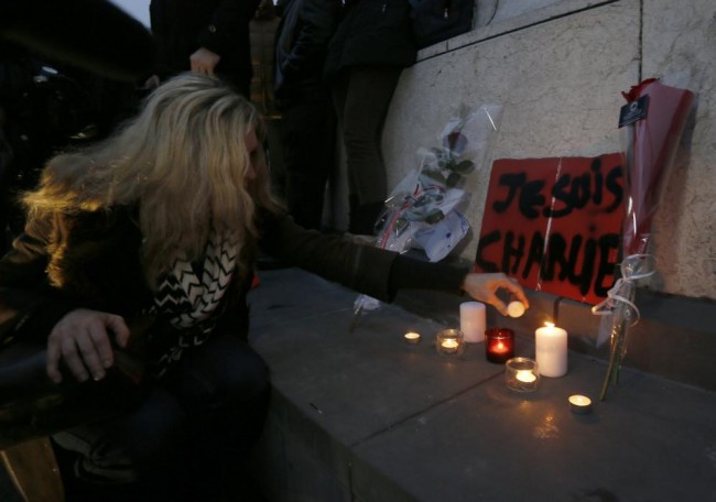 A woman places candles next to flowers and a placard which reads "I am Charlie" displayed to pay tribute during a gathering at the Place de la Republique in Paris