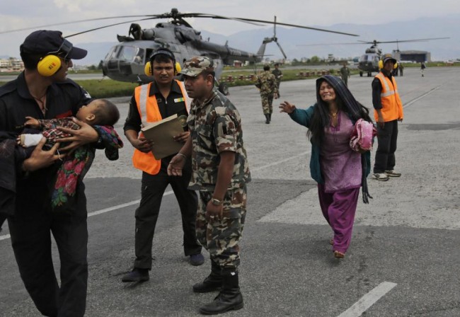 An Indian Air Force person walks carrying a Nepalese child, wounded in Saturdays earthquake, to a waiting ambulance as the mother rushes to join after they were evacuated from a remote area at the airport in Kathmandu, Nepal, Monday, April 27, 2015. The death toll from Nepal's earthquake is expected to rise depended largely on the condition of vulnerable mountain villages that rescue workers were still struggling to reach two days after the disaster.  (AP Photo/Altaf Qadri)