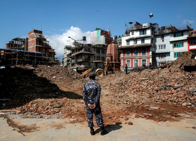 A member of Nepalese police personnel looks on as an excavator is used to dig through rubble to search for bodies, in the aftermath of Saturday's earthquake in Kathmandu, Nepal, April 27, 2015. REUTERS/Danish Siddiqui