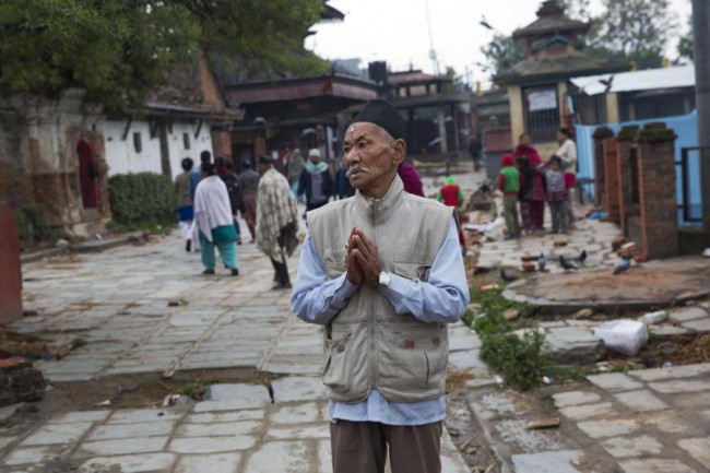 Un anciano nepalí reza junto a un edificio dañado (no fotografiado)en el terremoto que sacudió el país el sábado, en Katmandú, Nepal, el 27 de abril de 2015. (Foto AP/Bernat Armangue)