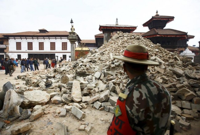 A Nepalese army personnel stands in front of a collapsed temple a day after an earthquake in Bhaktapur, Nepal April 26, 2015. Rescuers dug with their bare hands and bodies piled up in Nepal on Sunday after the earthquake devastated the heavily crowded Kathmandu valley, killing at least 1,900, and triggered a deadly avalanche on Mount Everest.  REUTERS/Navesh Chitrakar